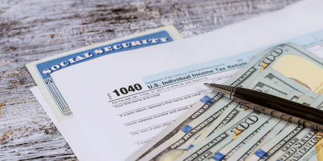 Tax return documents sit atop a table along with a stack of money and an ink pen