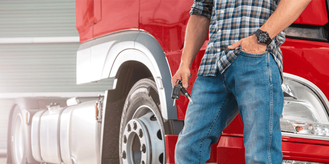 Truck driver stands and holds keys beside parked semi-truck tractor