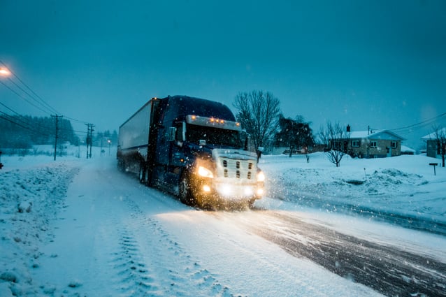Semi-truck driving on a dark, snowy road