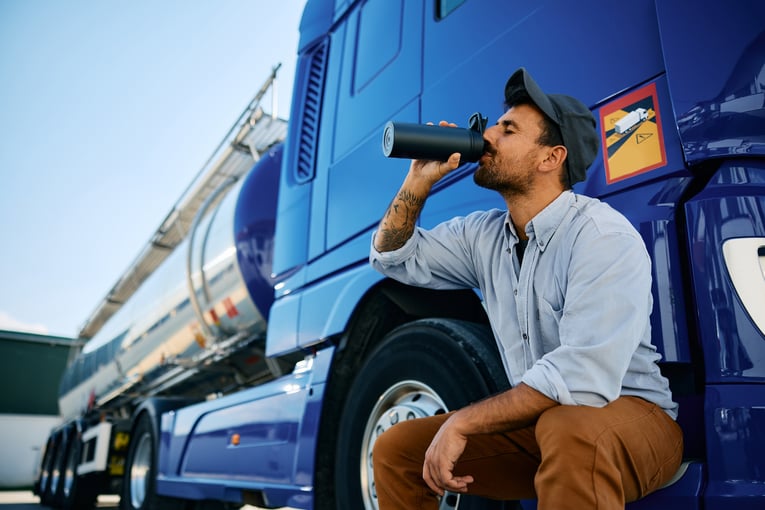 A truck driver sits outside his semi drinking a water bottle in hot weather